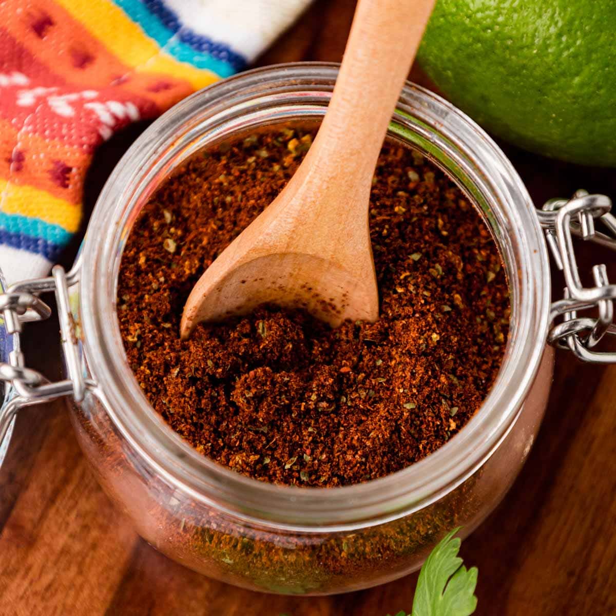 Homemade elote seasoning in a glass jar with a wooden spoon.