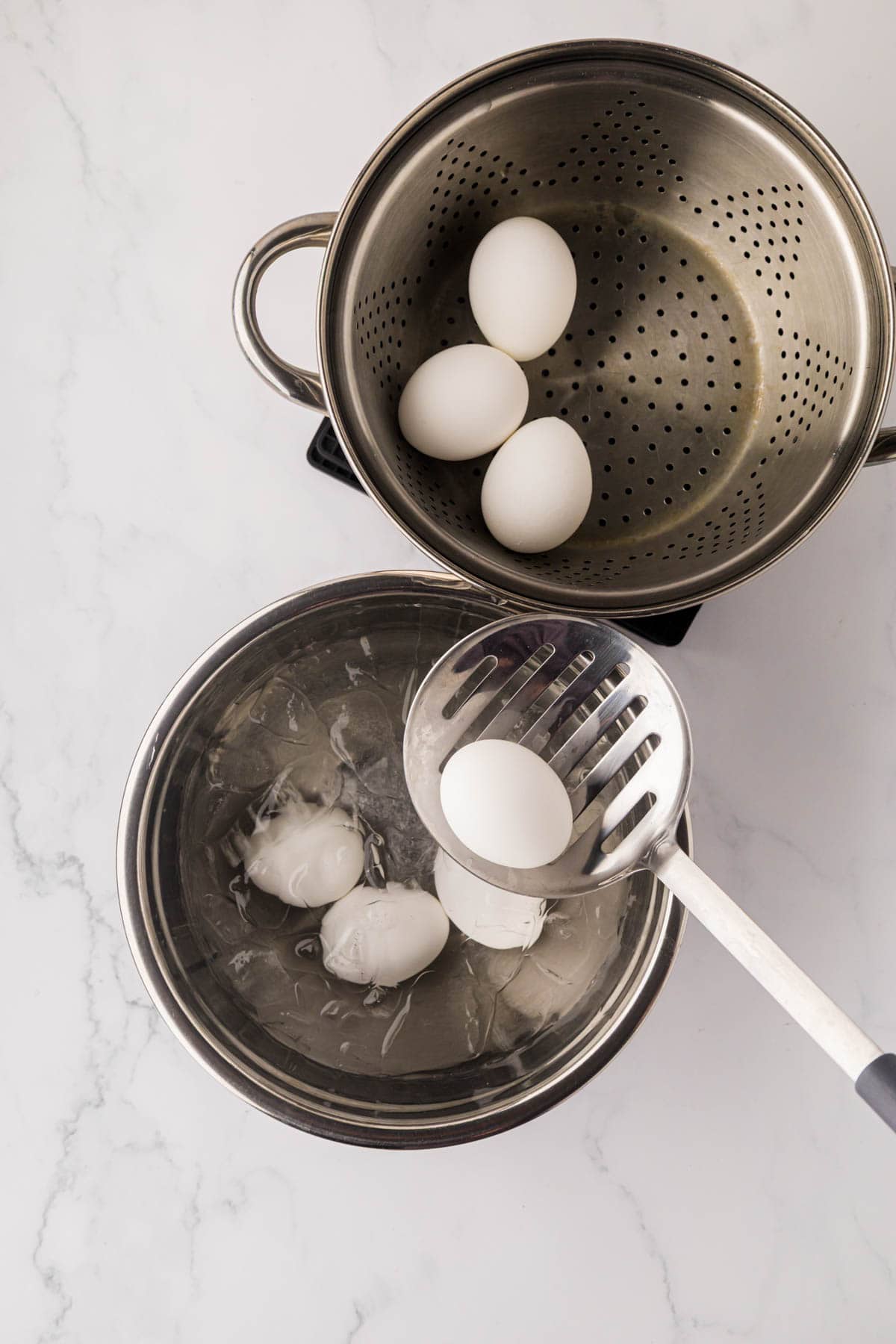 Transferring boiled eggs from steamer to an ice water bath.