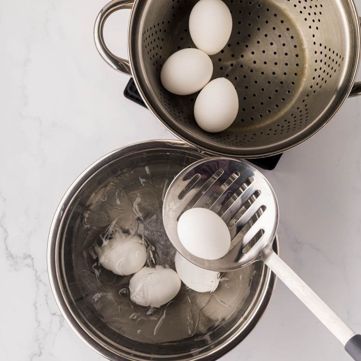 Transferring boiled eggs from steamer to an ice water bath.