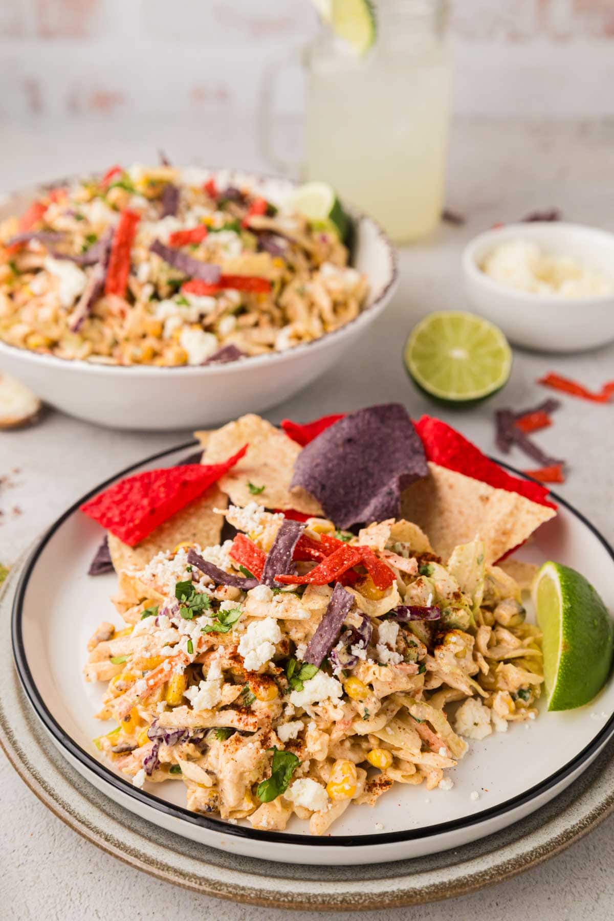 A plate of street corn coleslaw garnished with tortilla chips and lime.