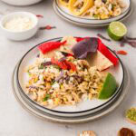 A plate of street corn coleslaw garnished with tortilla chips and lime.