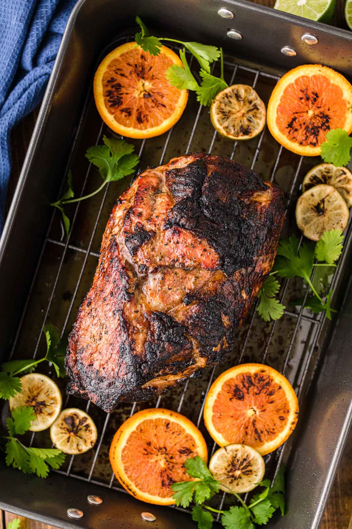Roasted Cuban style pork on a roasting pan with slices of citrus and cilantro around it.