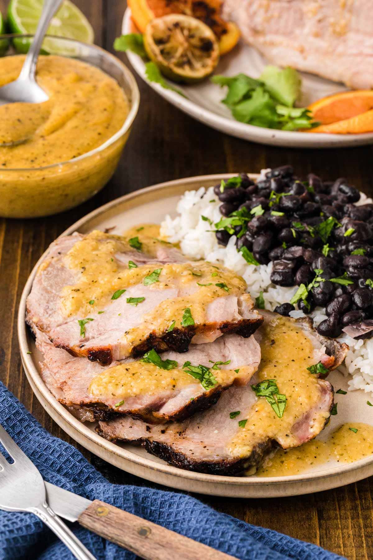 Slices of roasted Cuban pork on a plate served with rice and black beans.