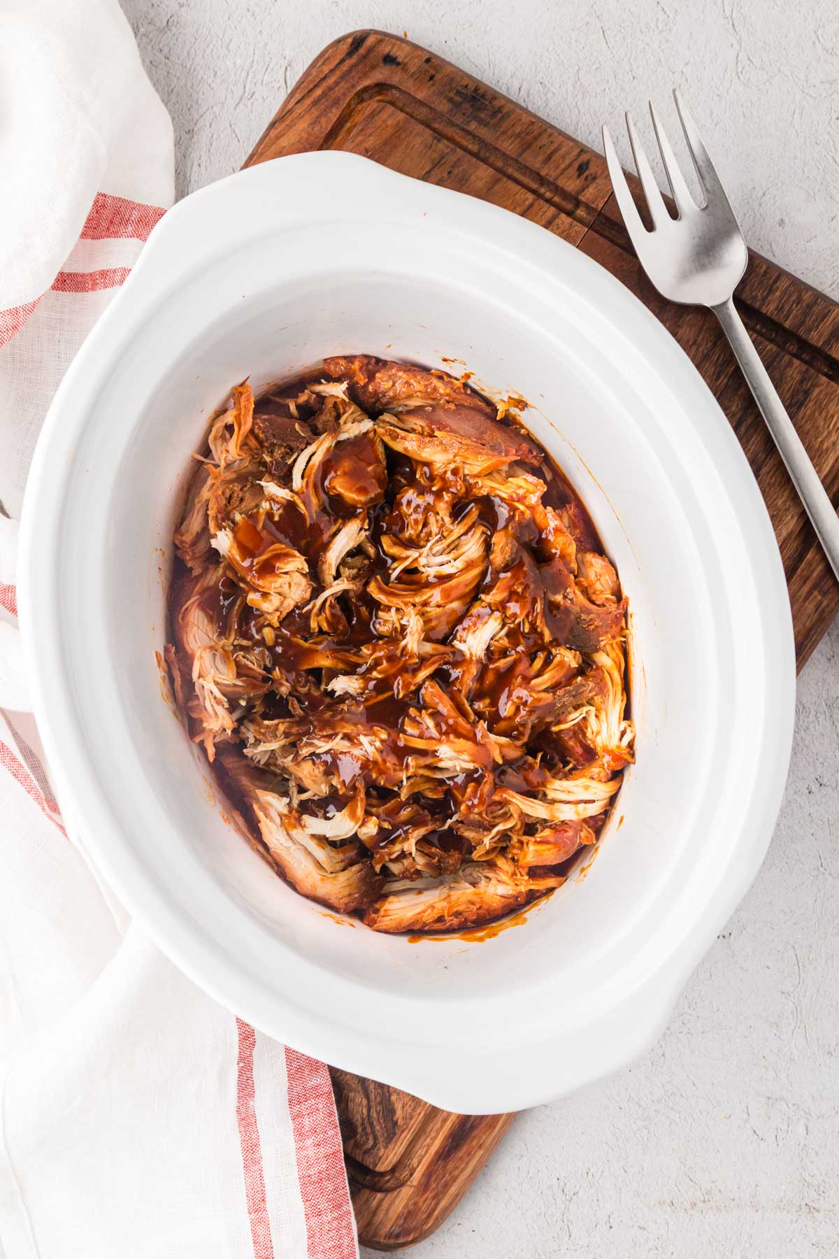 Slow cooker pulled BBQ chicken in a white crock pot.