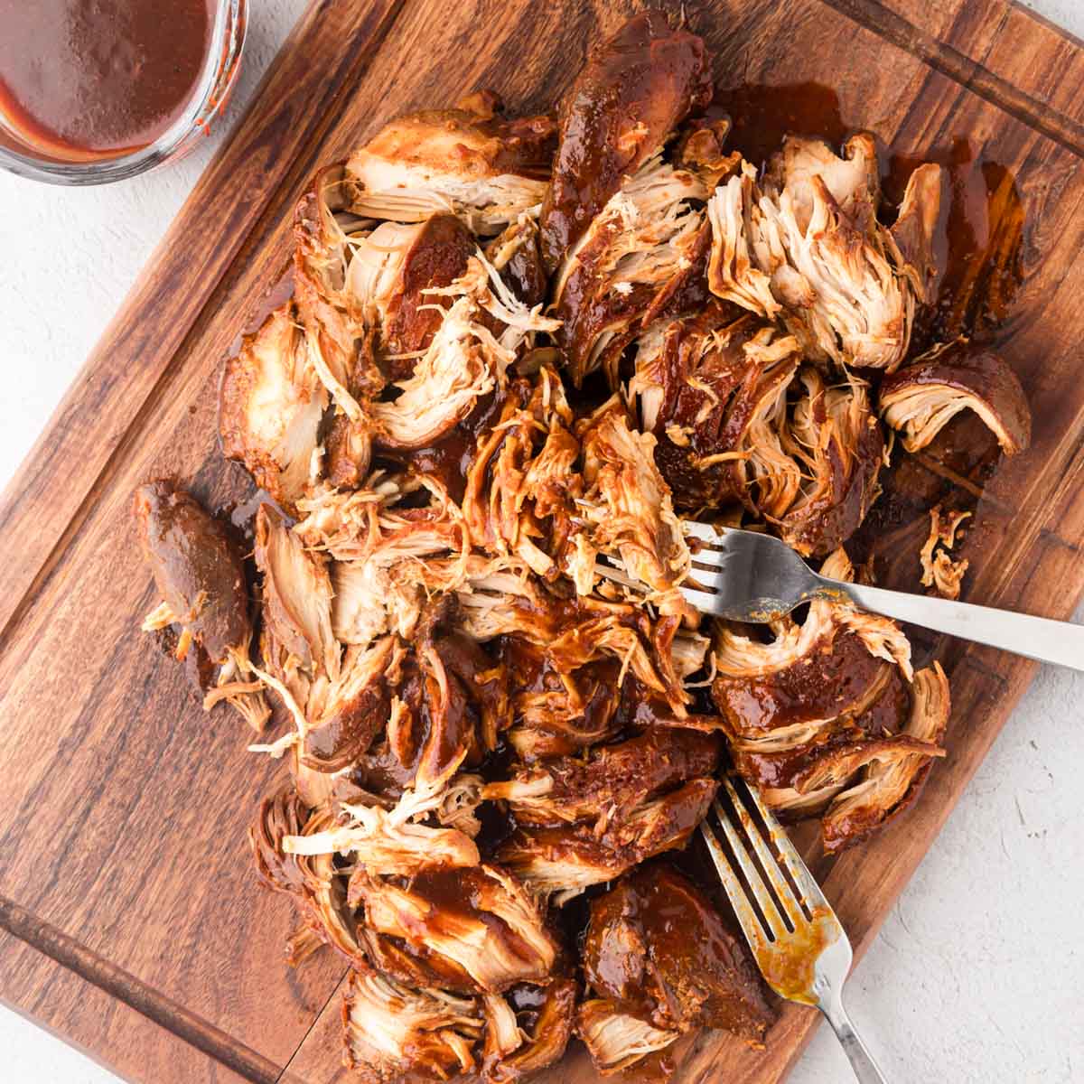 Shredded BBQ chicken with two forks on a wooden board.