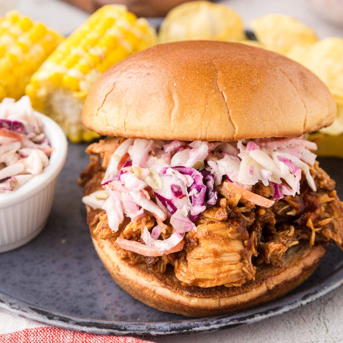 Slow cooker pulled BBQ chicken served as a sandwich on a plate with sides.