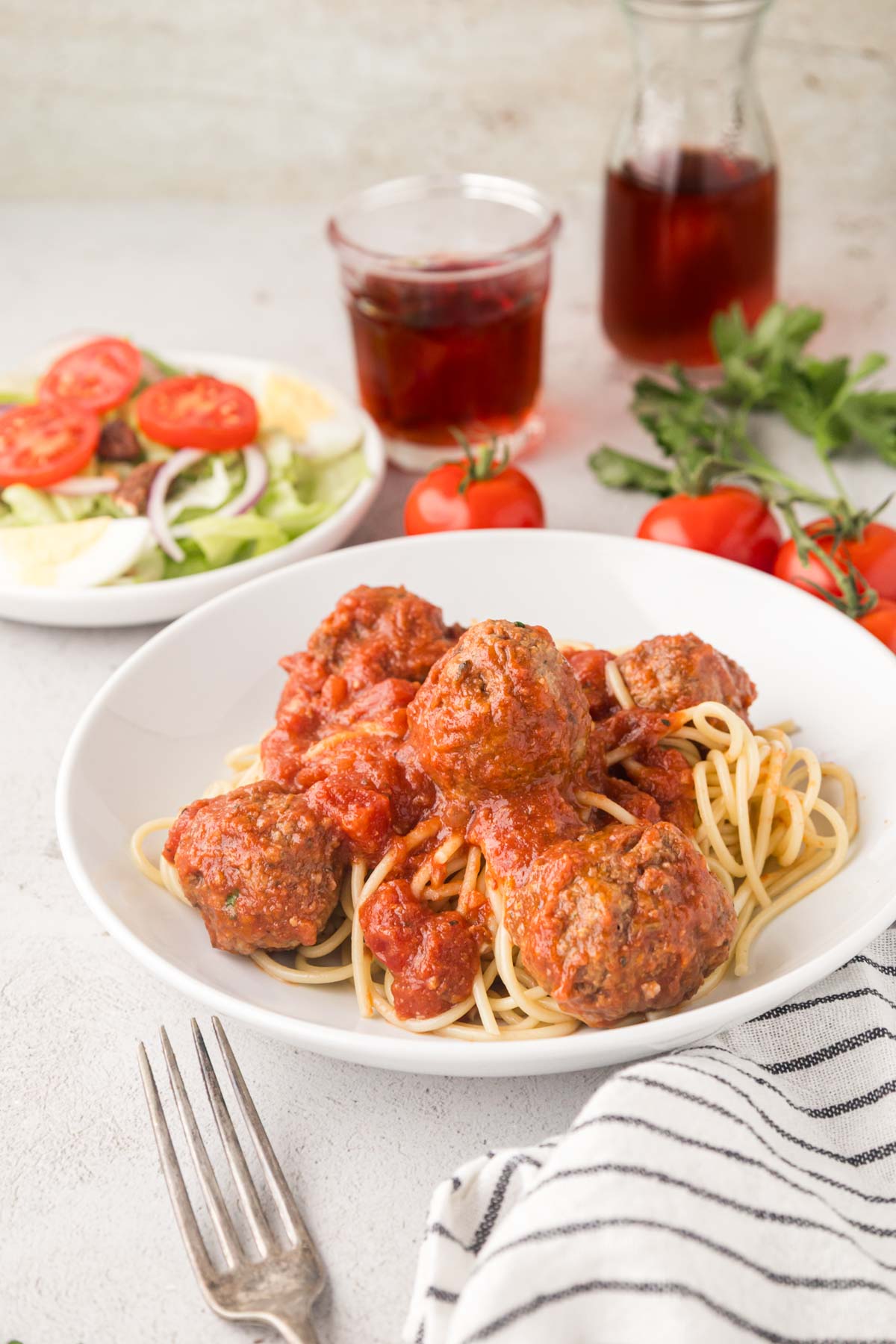 Slow cooker meatballs served on a bet of spaghetti in a white bowl.