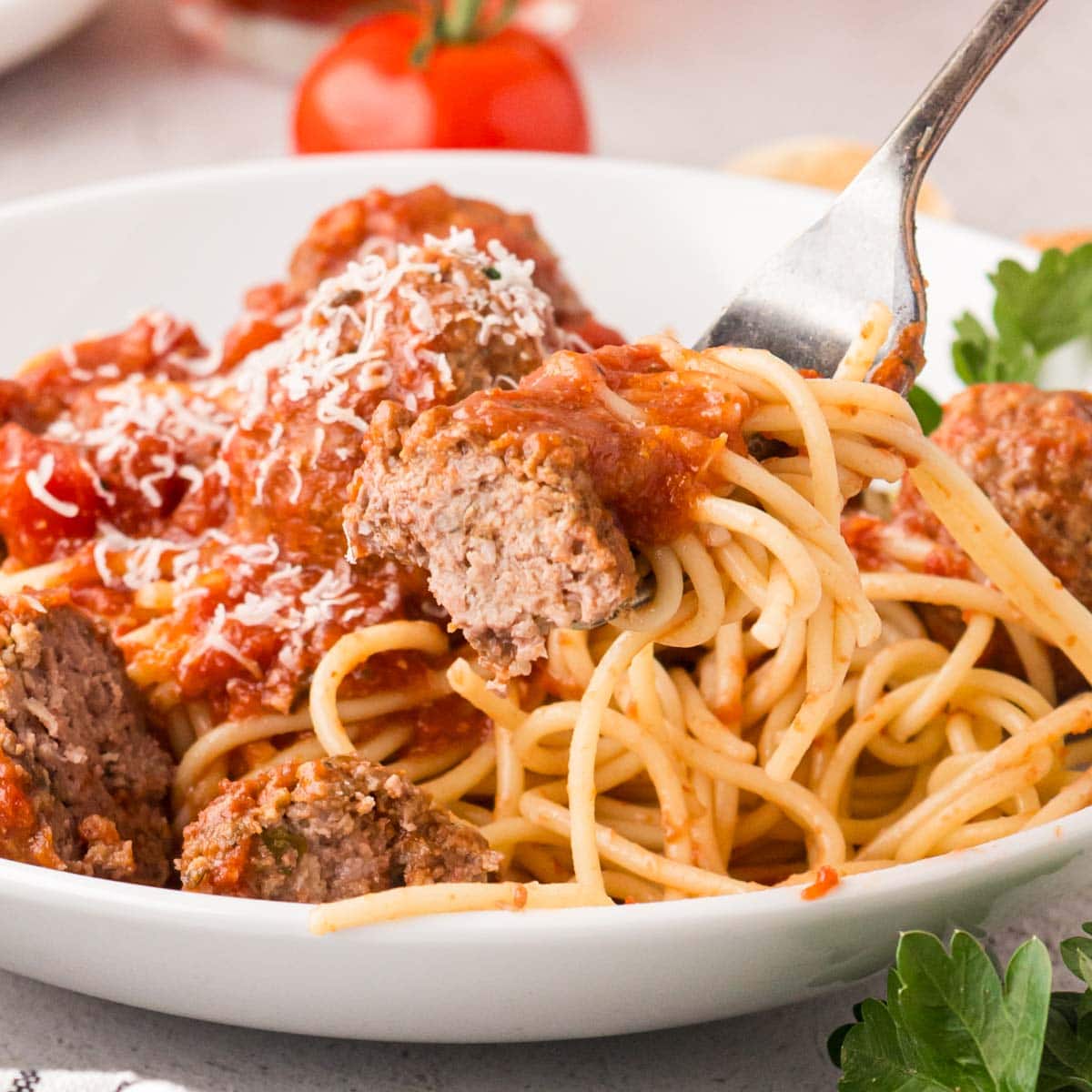 Fork scooping up a bite of Italian meatballs with sauce and noodles in a bowl.