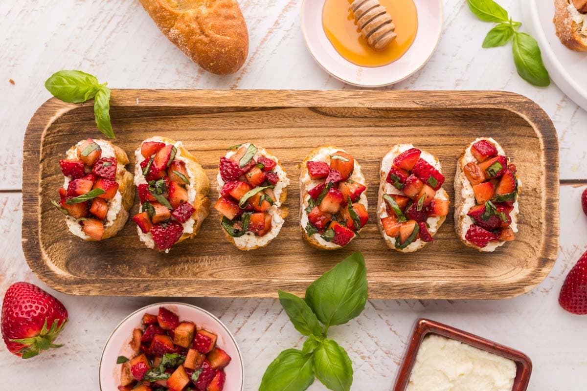 Overhead shot of strawberry ricotta bruschetta served on a wooden serving platter.