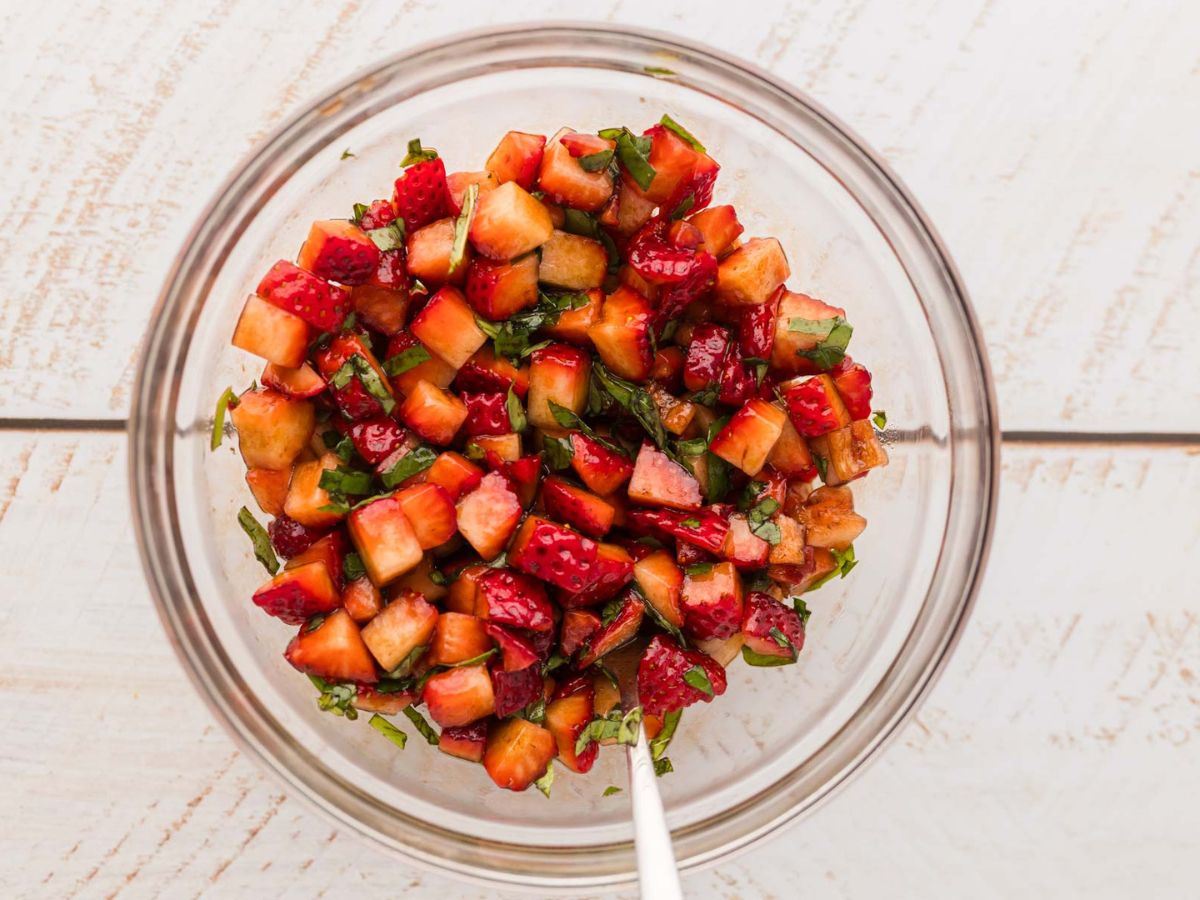 Diced strawberries mixed with basil, olive oil, and balsamic vinegar in a mixing bowl.