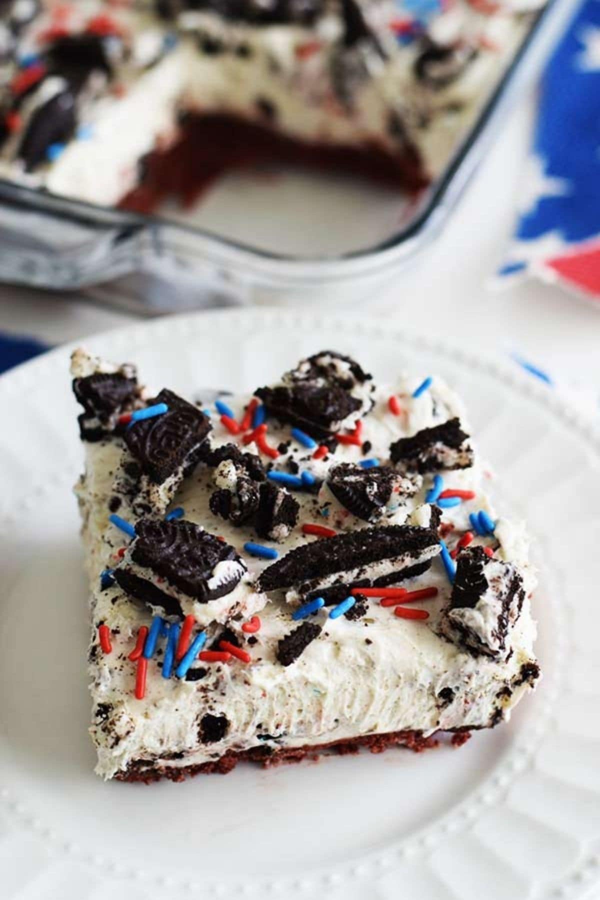 A slice of a no bake fireworks Oreo cheesecake bar with red, white, and blue sprinkles and chopped Oreos on top.