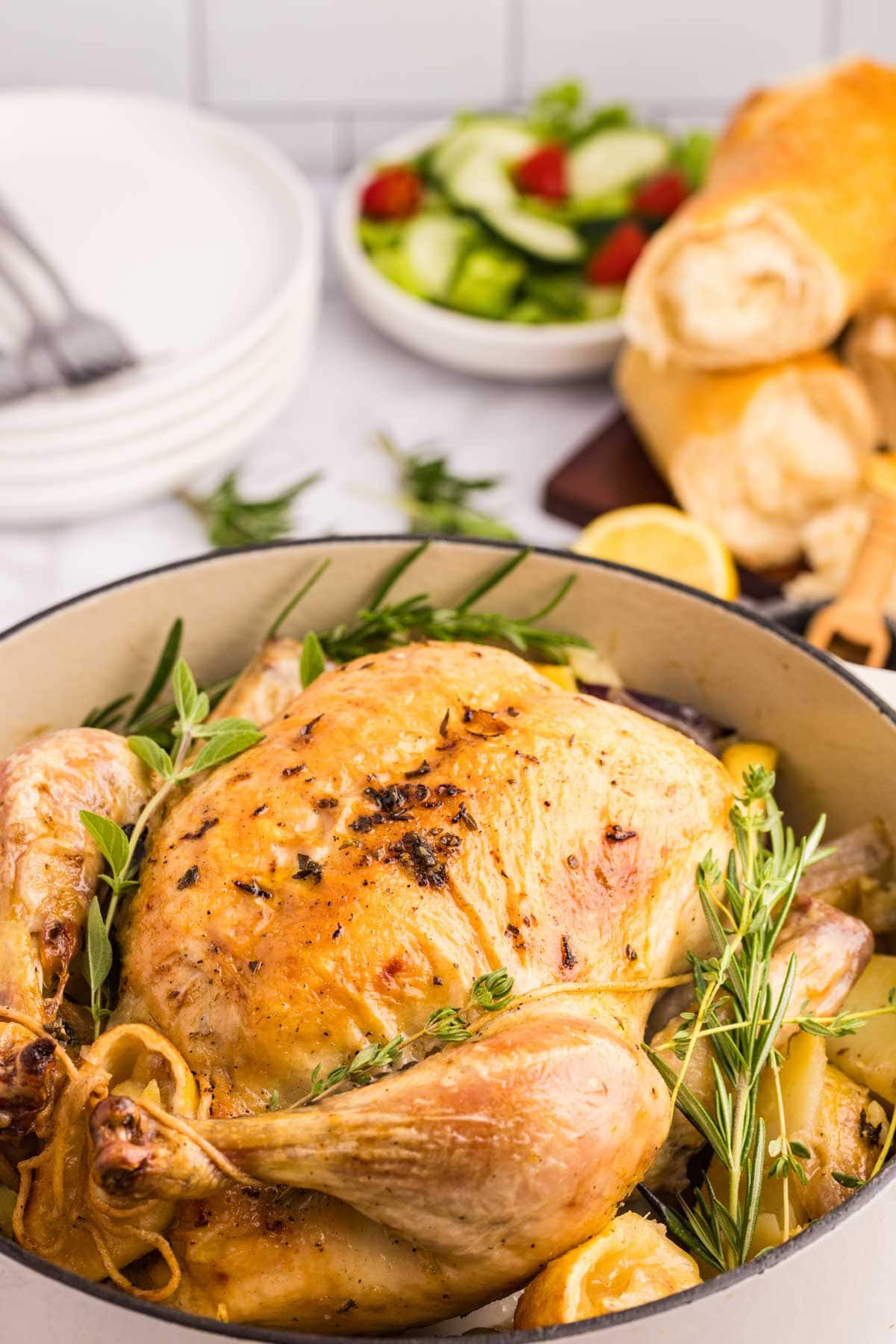Greek roasted chicken in a Dutch oven on a bed of potatoes and onions.