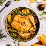 Greek roast chicken in a Dutch oven garnished with fresh herbs.