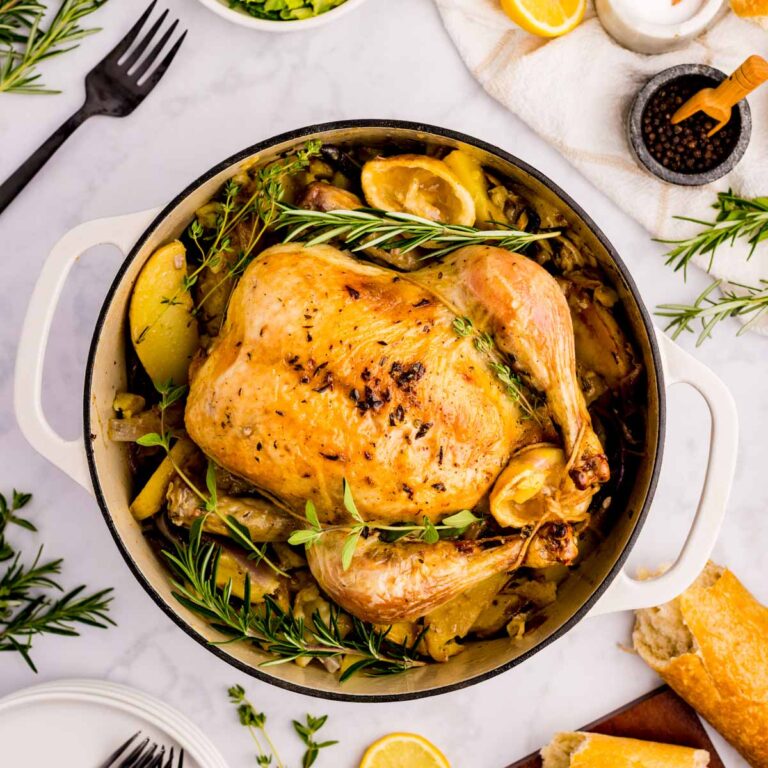 Greek roast chicken in a Dutch oven garnished with fresh herbs.