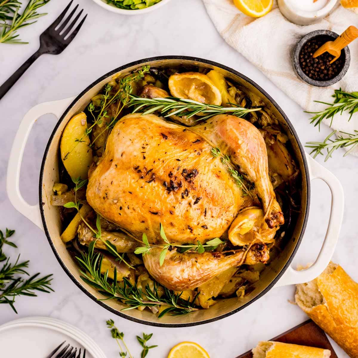 Greek roast chicken in a Dutch oven garnished with fresh herbs.
