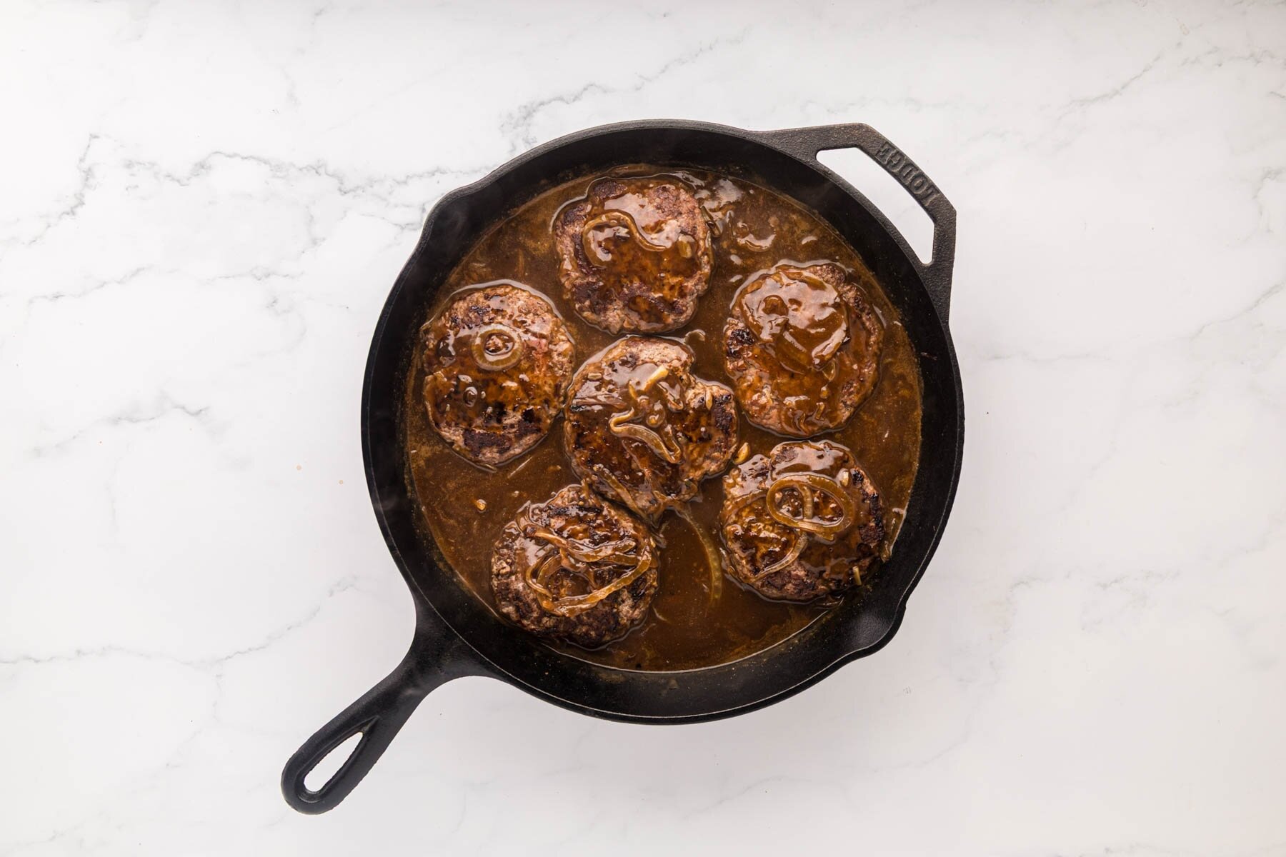 hamburger steaks covered in gravy in a cast iron skillet.