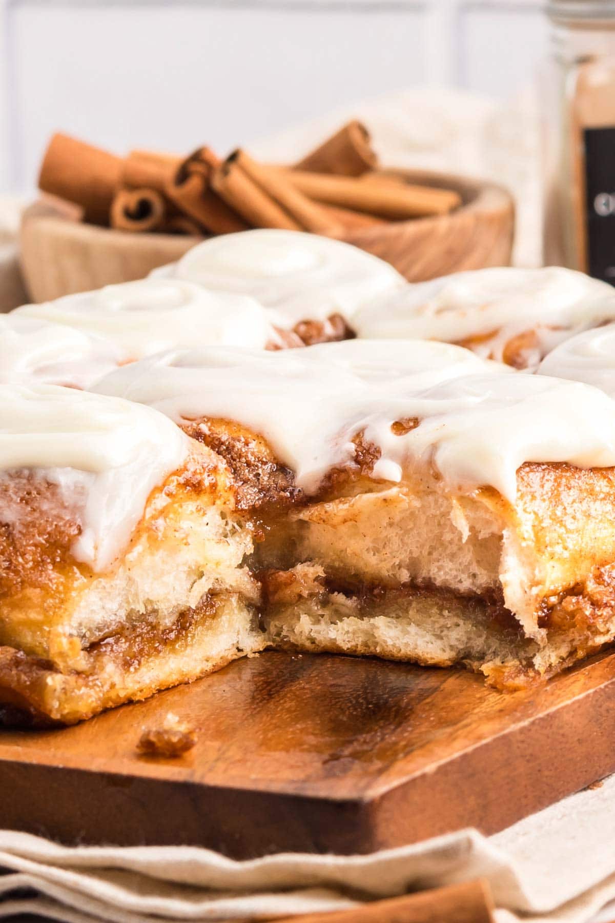 Hawaiian roll cinnamon rolls on a wooden board with one missing to show the inside layers.