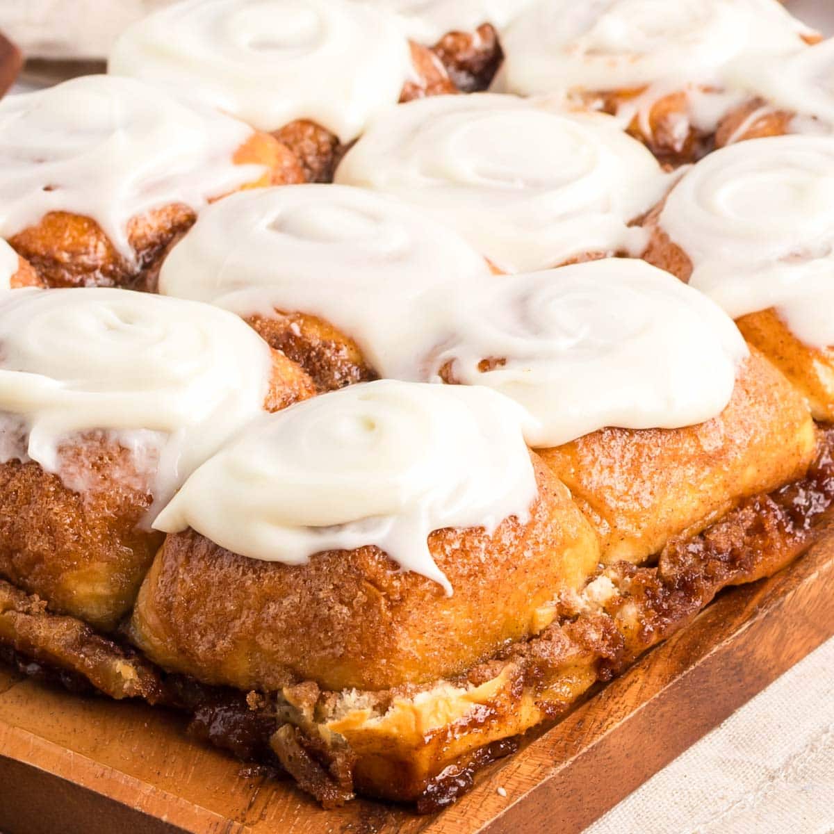 Hawaiian roll cinnamon rolls on a wooden board topped with cream cheese frosting.