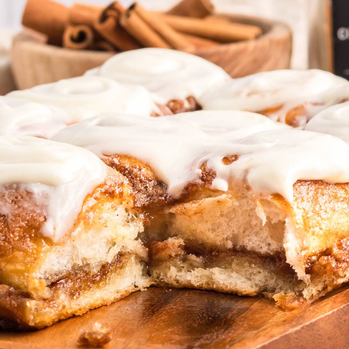Side view of Hawaiian roll cinnamon rolls on a wooden board with one missing.