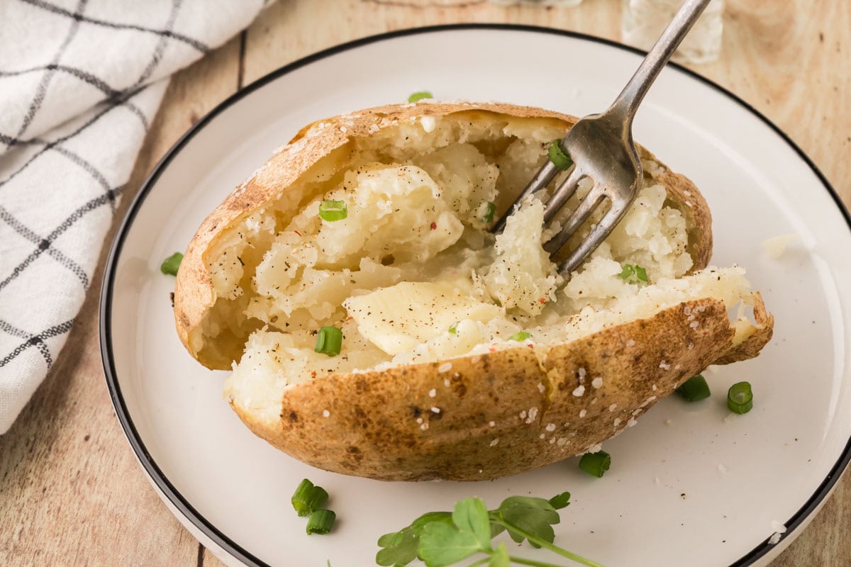 A fork fluffing the inside of a baked potato.