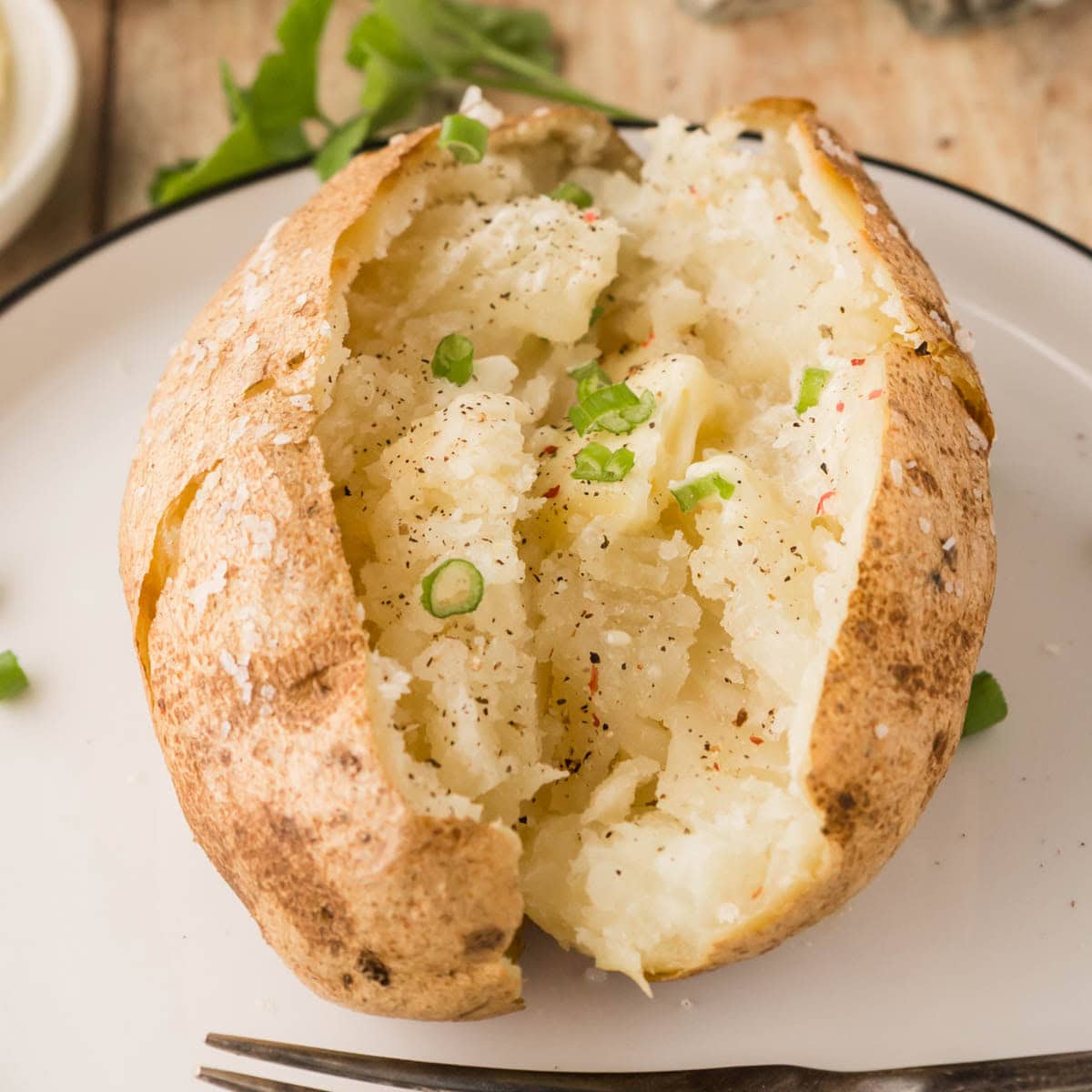 A baked potato garnished with chives and sprinkled with red pepper.