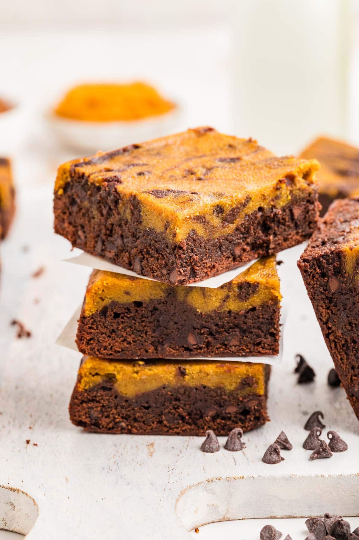 Pumpkin brownies stacked on top of each other with chocolate chips scattered around.