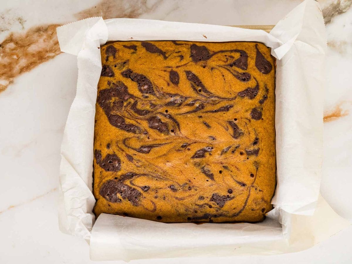 Baked pumpkin brownies in a parchment lined brownie pan.