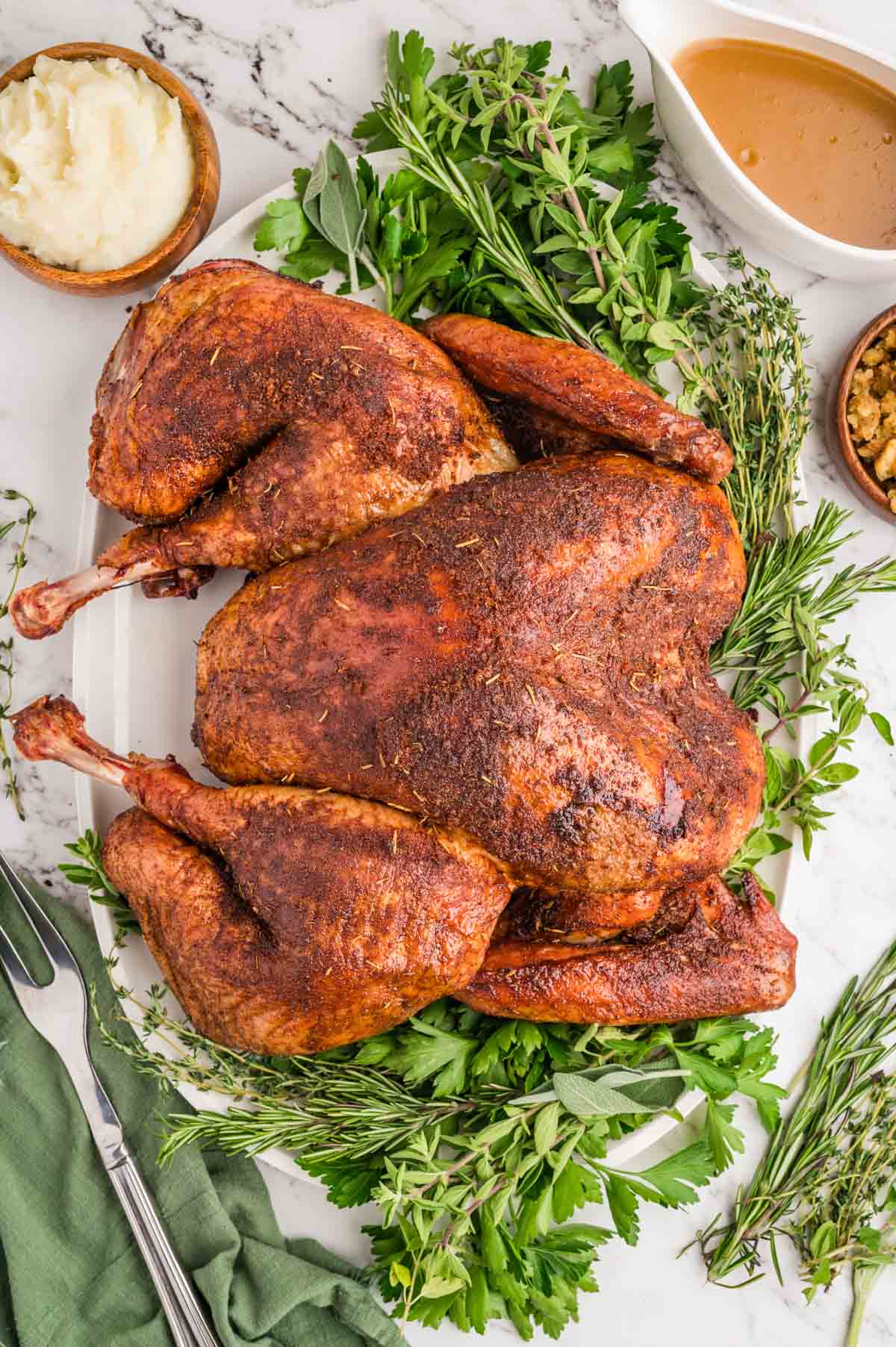 Smoked spatchcock turkey served on a serving plate with herbs and gravy on the side.