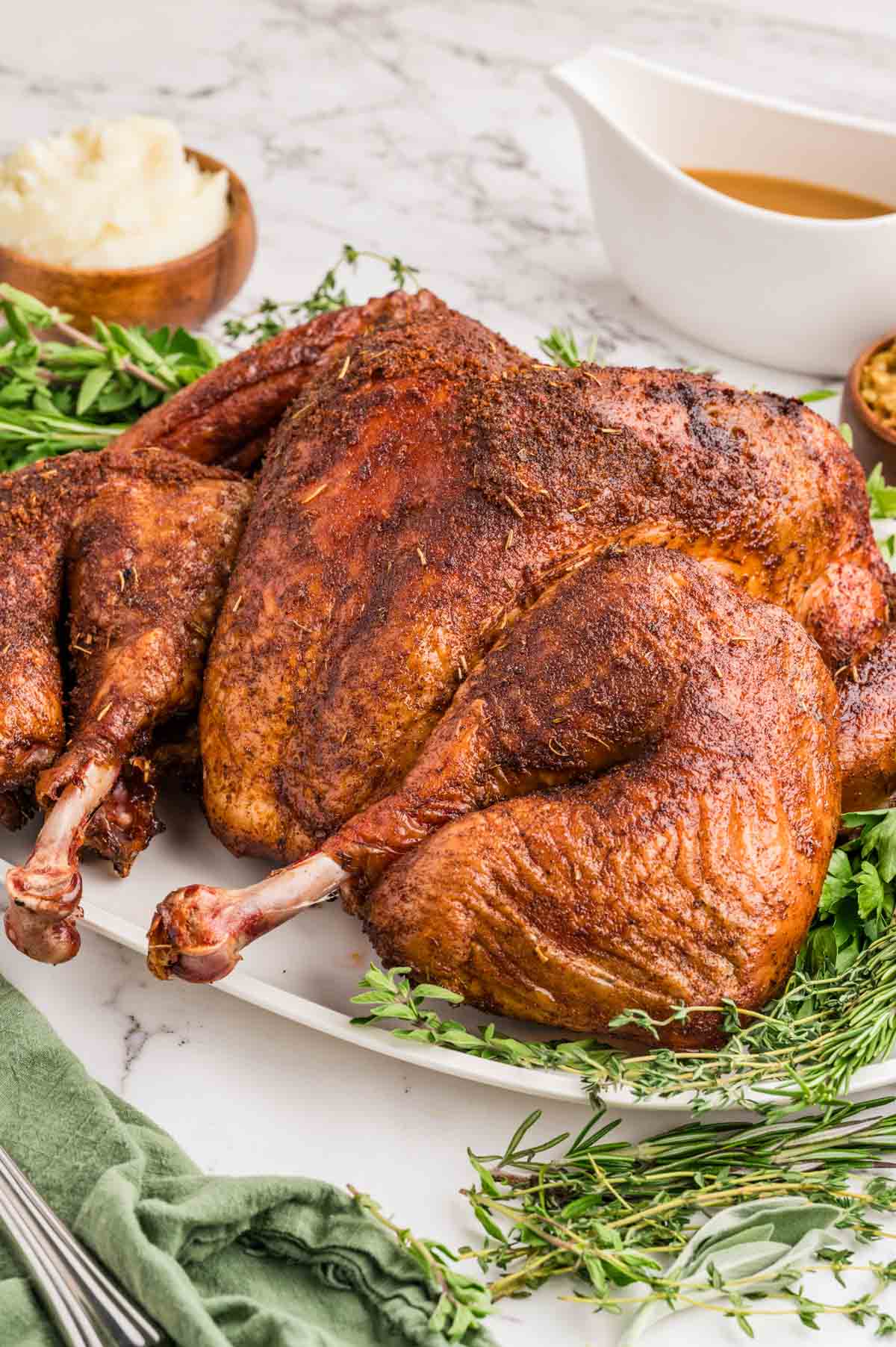 Smoked spatchcock turkey on a shite serving plate with fresh herbs.