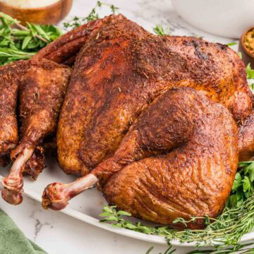 Side view of smoked spatchcock turkey on a bed of herbs on a platter.