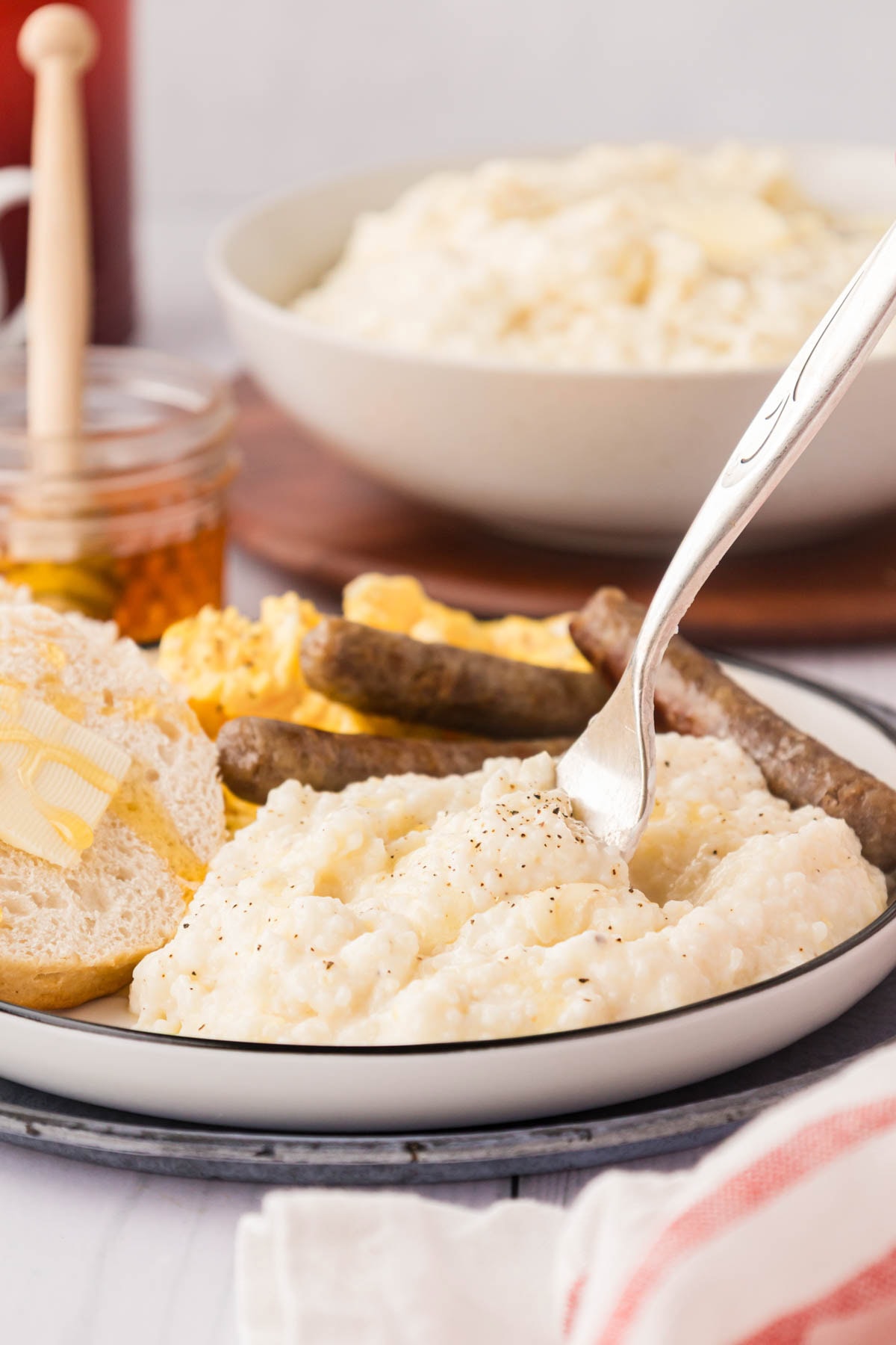 A plate with breakfast grits, sausage, eggs, and biscuits.