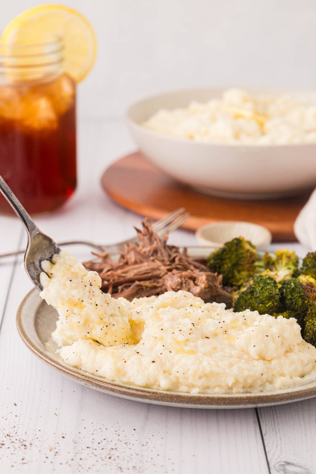 Grits on a plate with roast and broccoli.