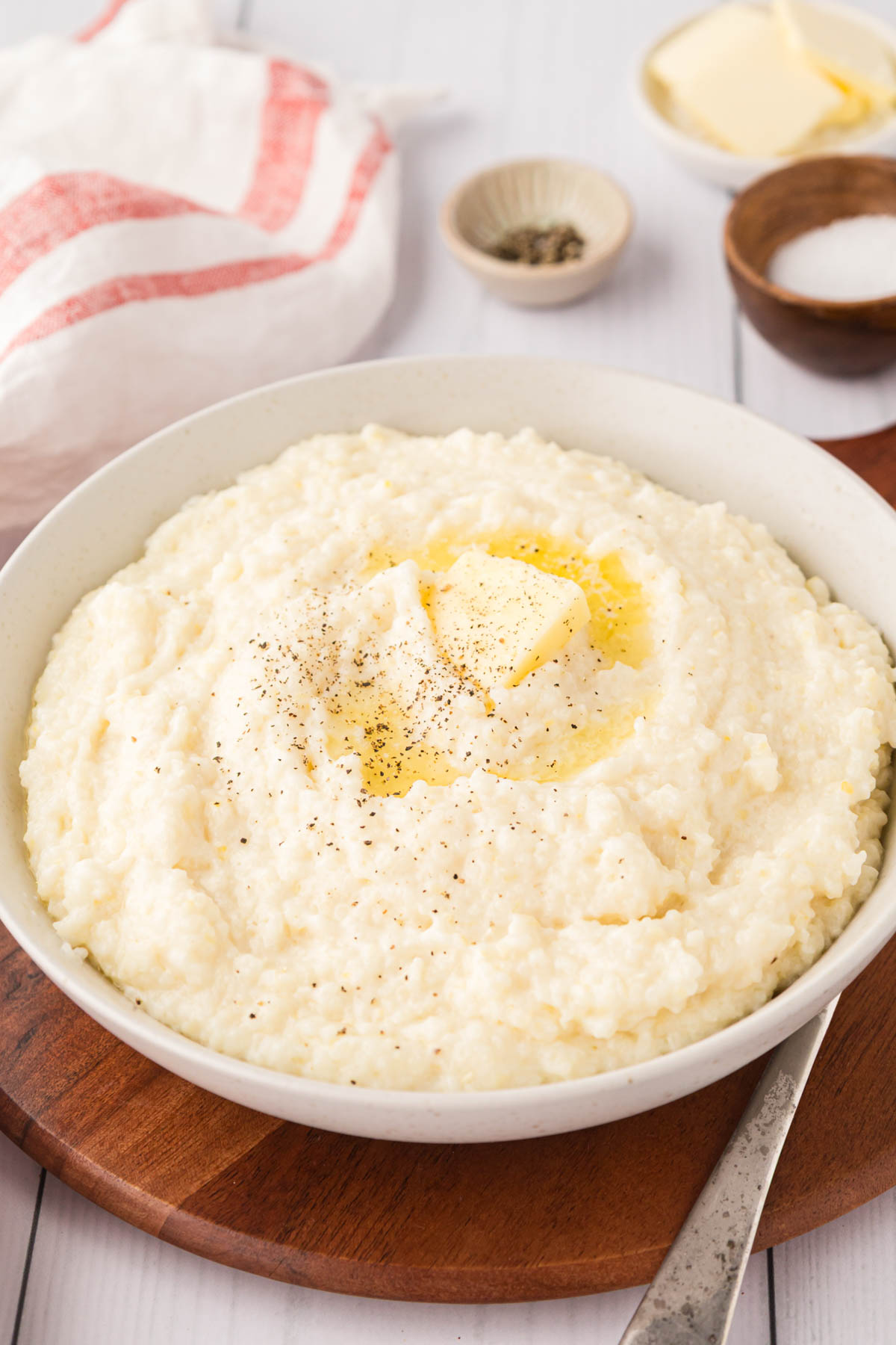 Creamy grits with butter and pepper on top served in a white bowl.