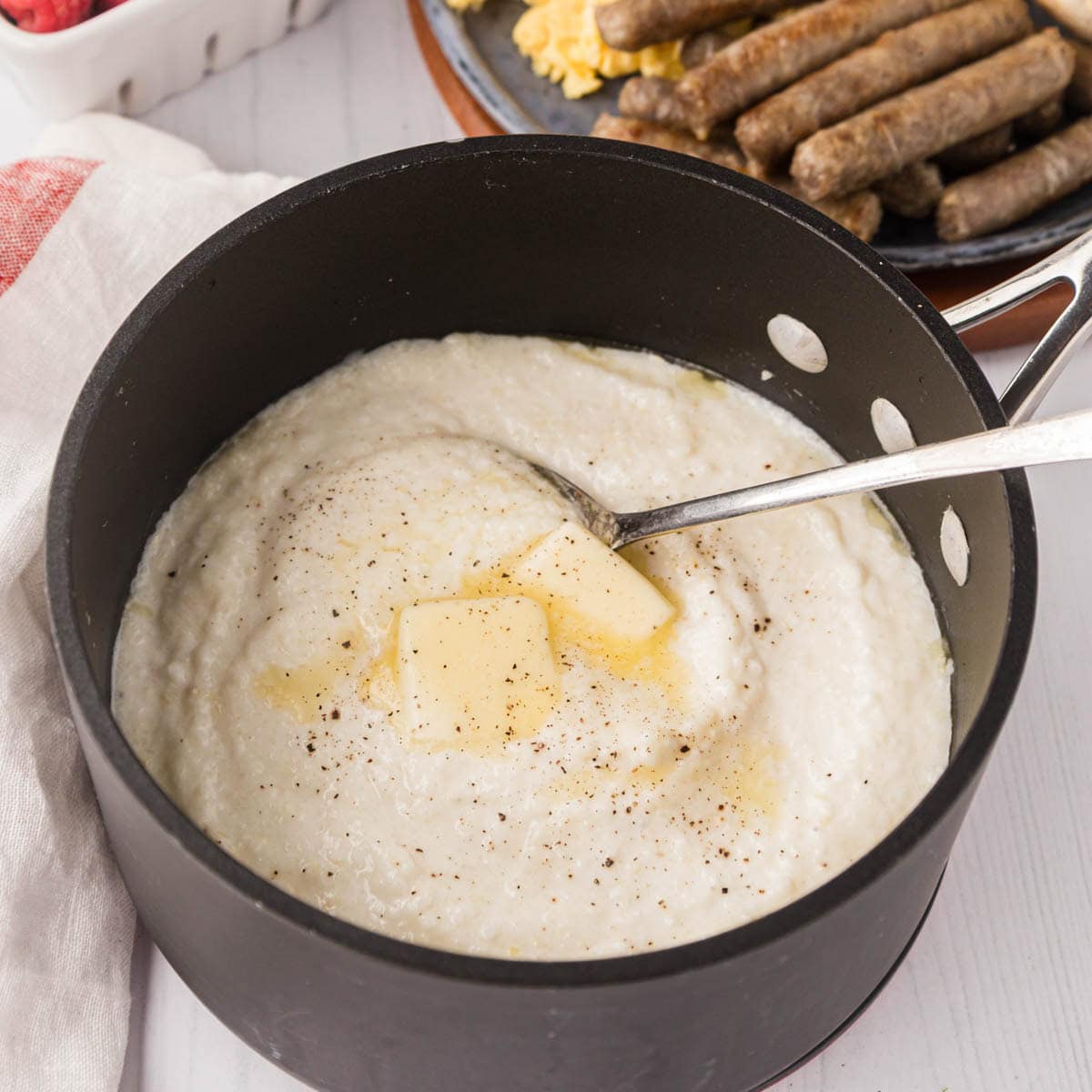 Grits in a pot with a platter of eggs, sausage and biscuits in the background.