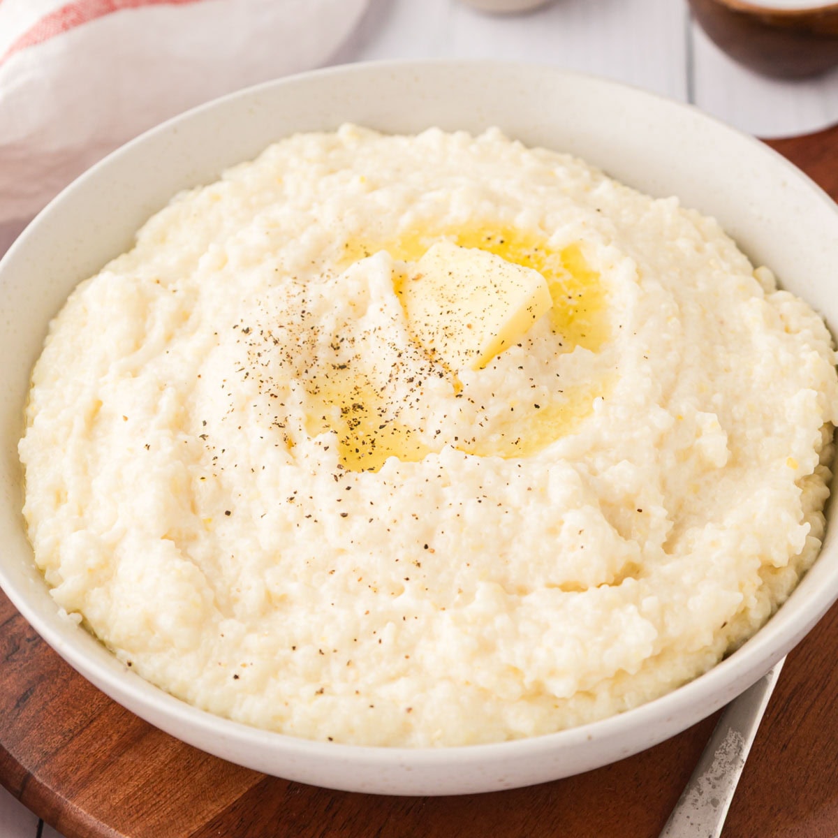 Creamy grits with butter and pepper on top served in a white bowl.