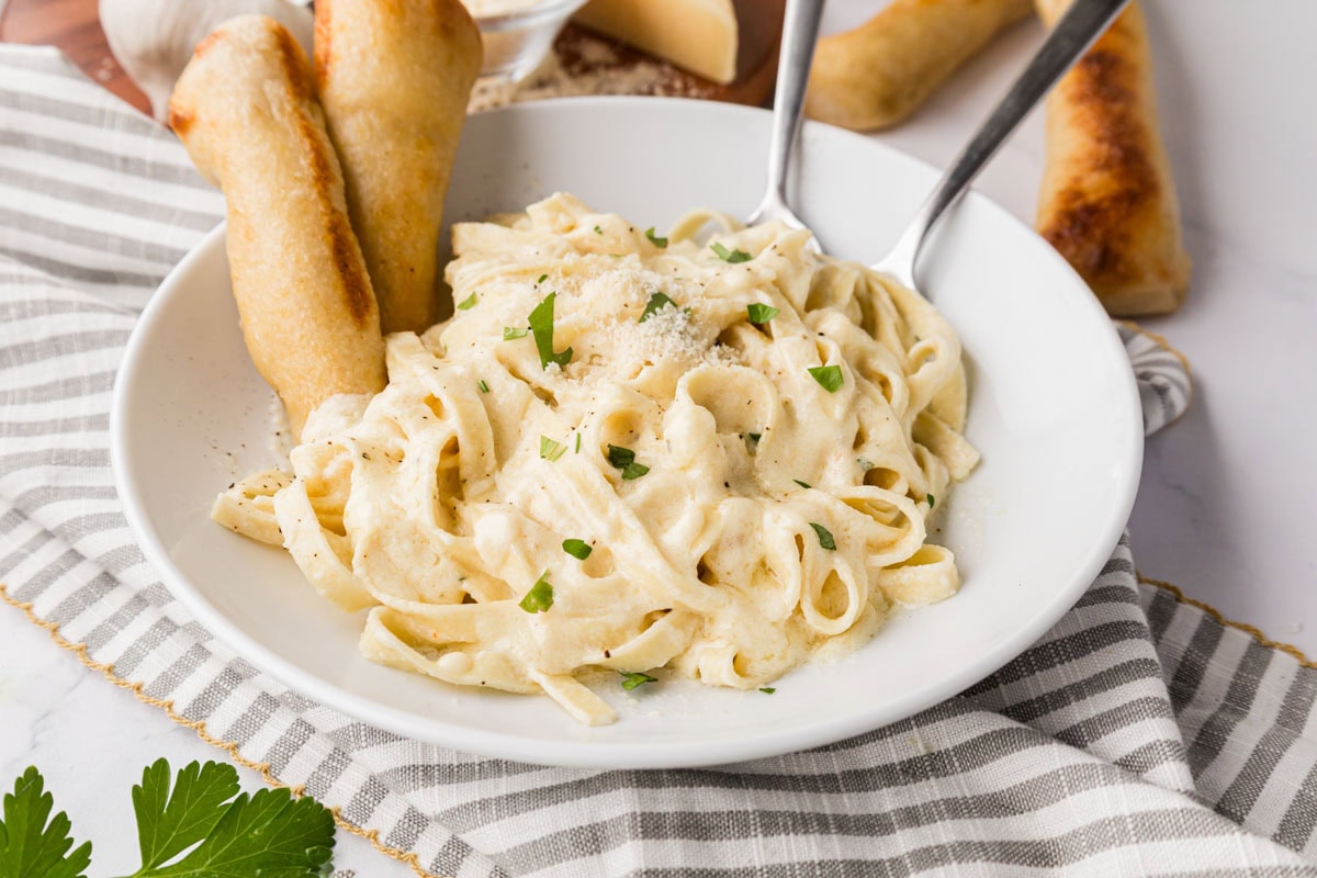 A white bowl filled with fettuccine noodles with Alfredo sauce.