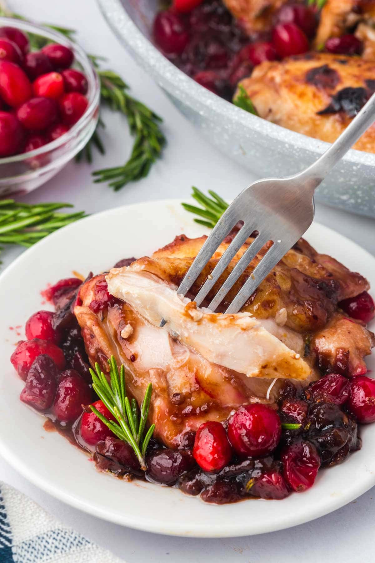 Fork taking a bite of the balsamic cranberry chicken on a plate.