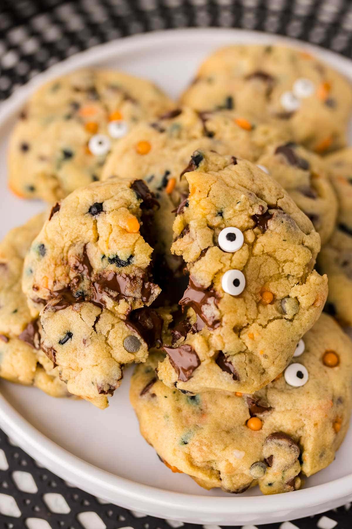 Halloween chocolate chip cookies on a plate with one broken in half on top.