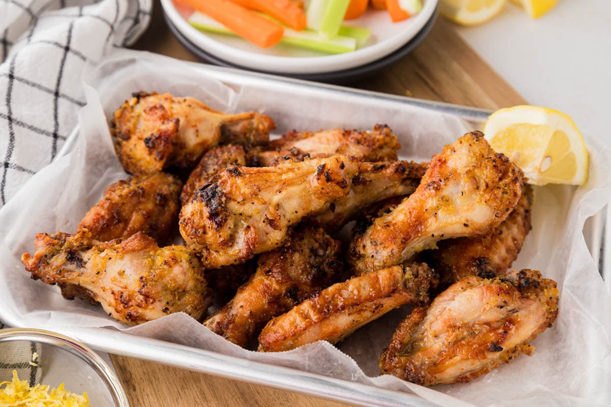Lemon pepper chicken wings on a parchment line tray served with lemon wedge.
