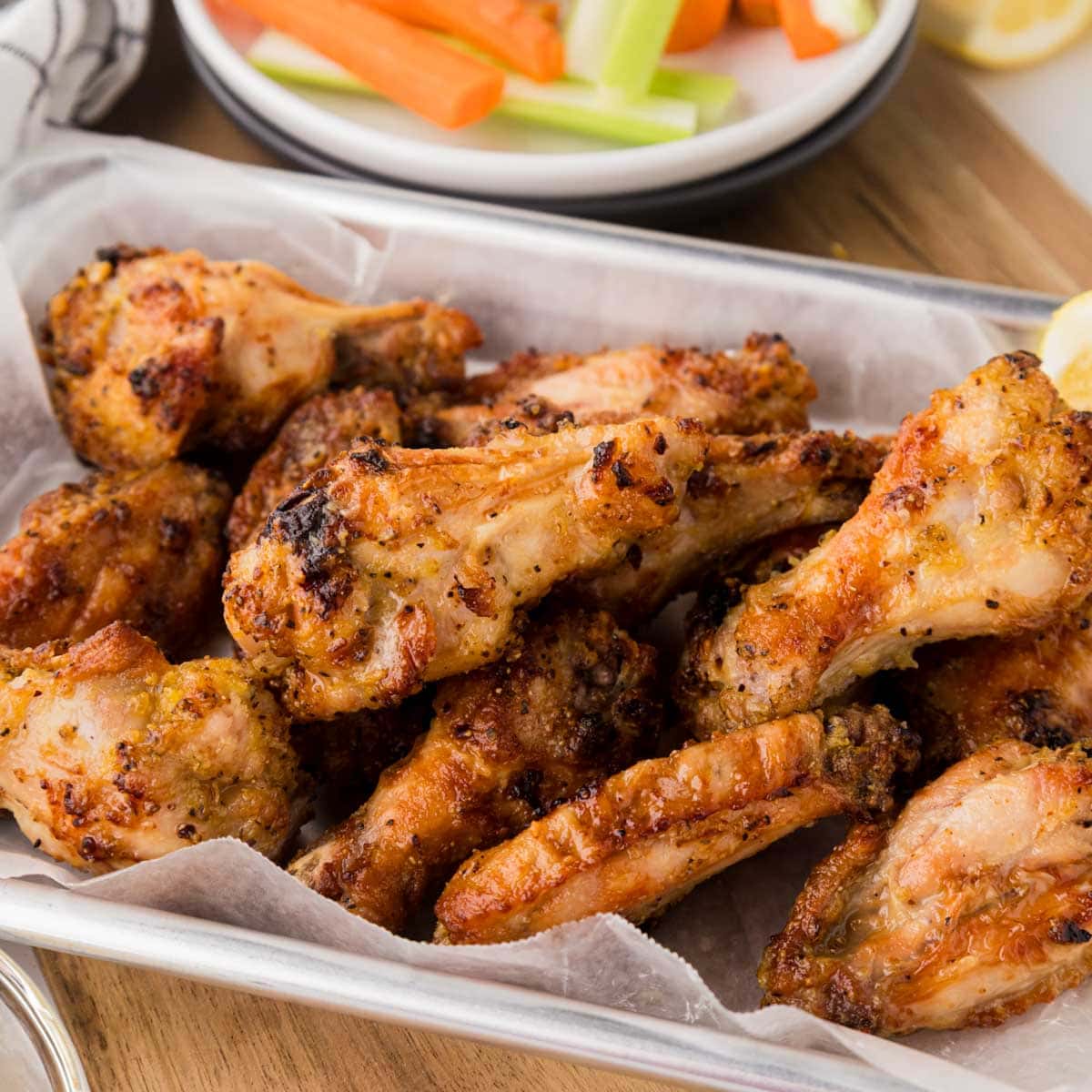 Lemon pepper chicken wings on a parchment line tray served with lemon wedge.