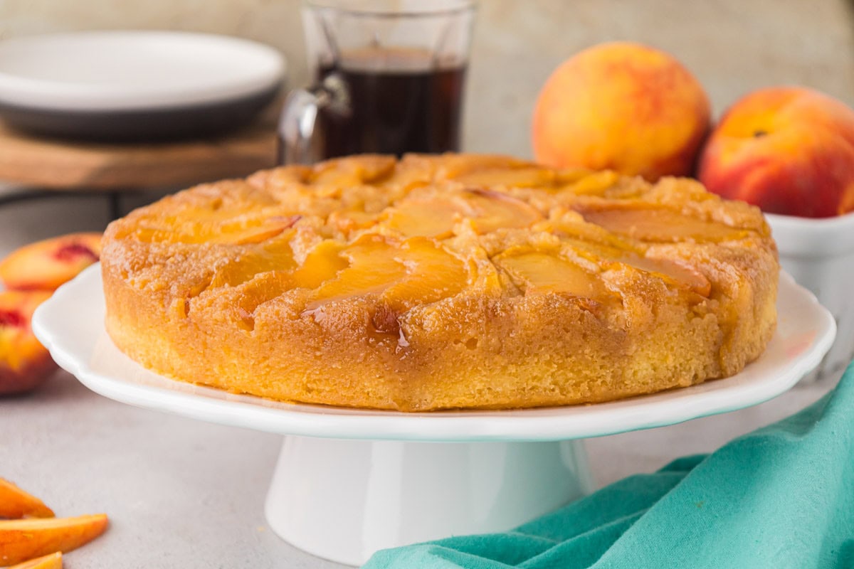 A side view image of the peach upside down cake on a cake stand.