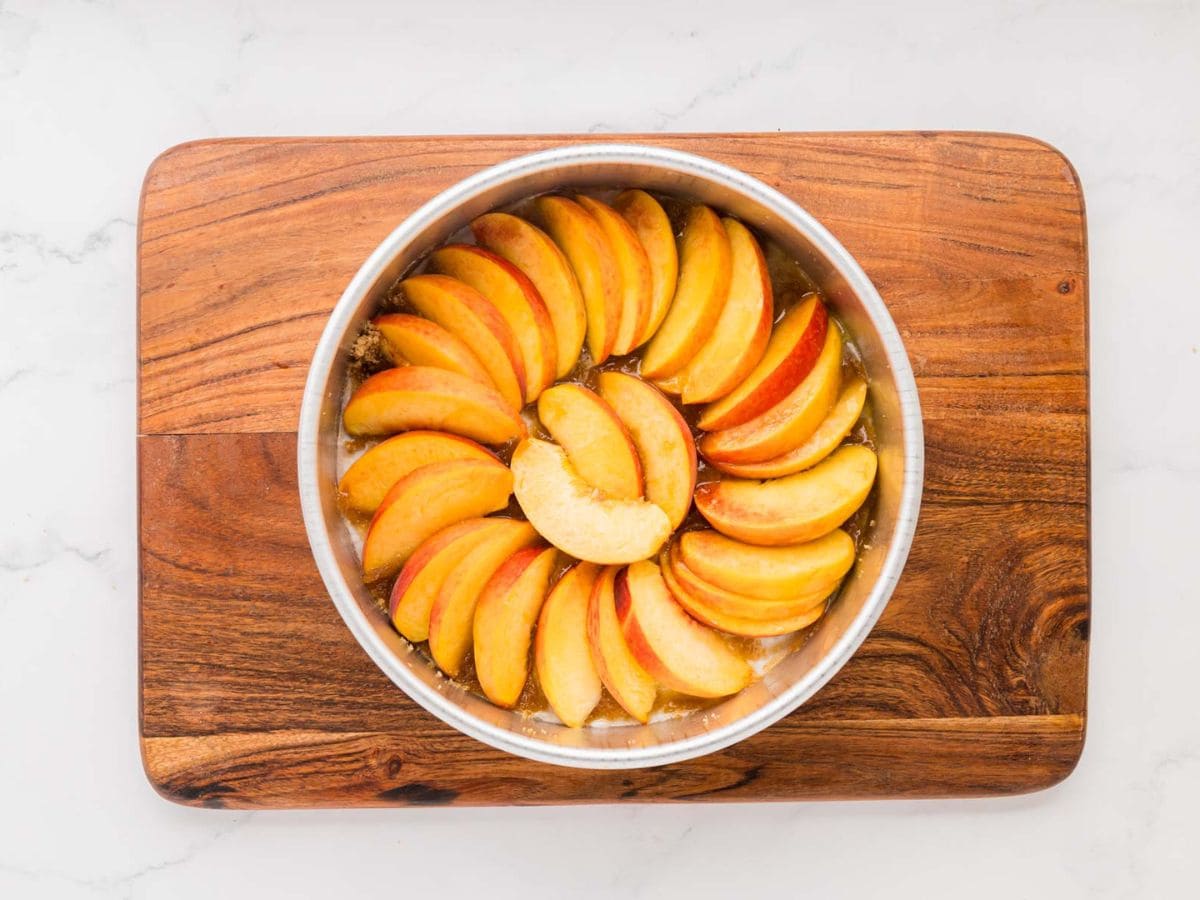 Sliced peaches in the bottom of a round cake pan in a circular pattern.