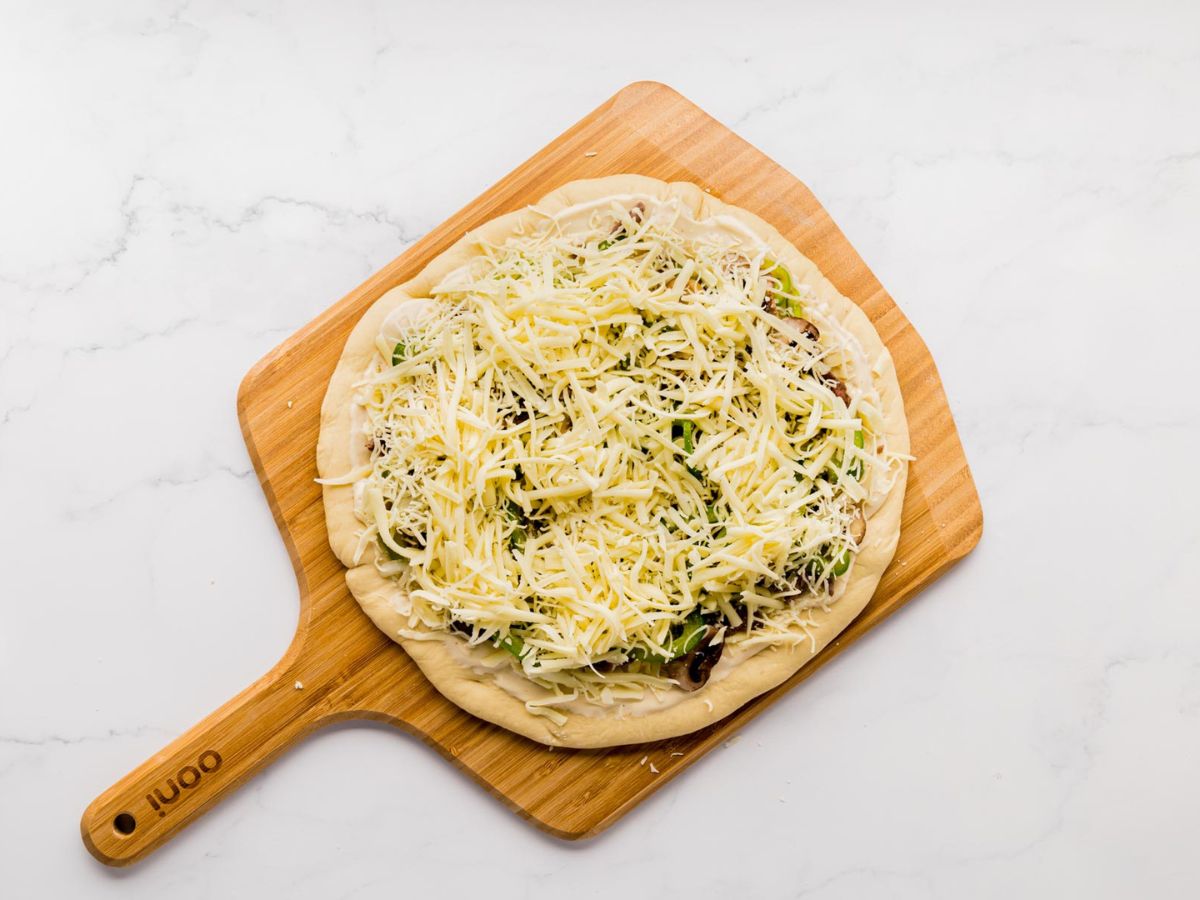 A Philly cheesesteak pizza with the final layer of cheese on top before baking.