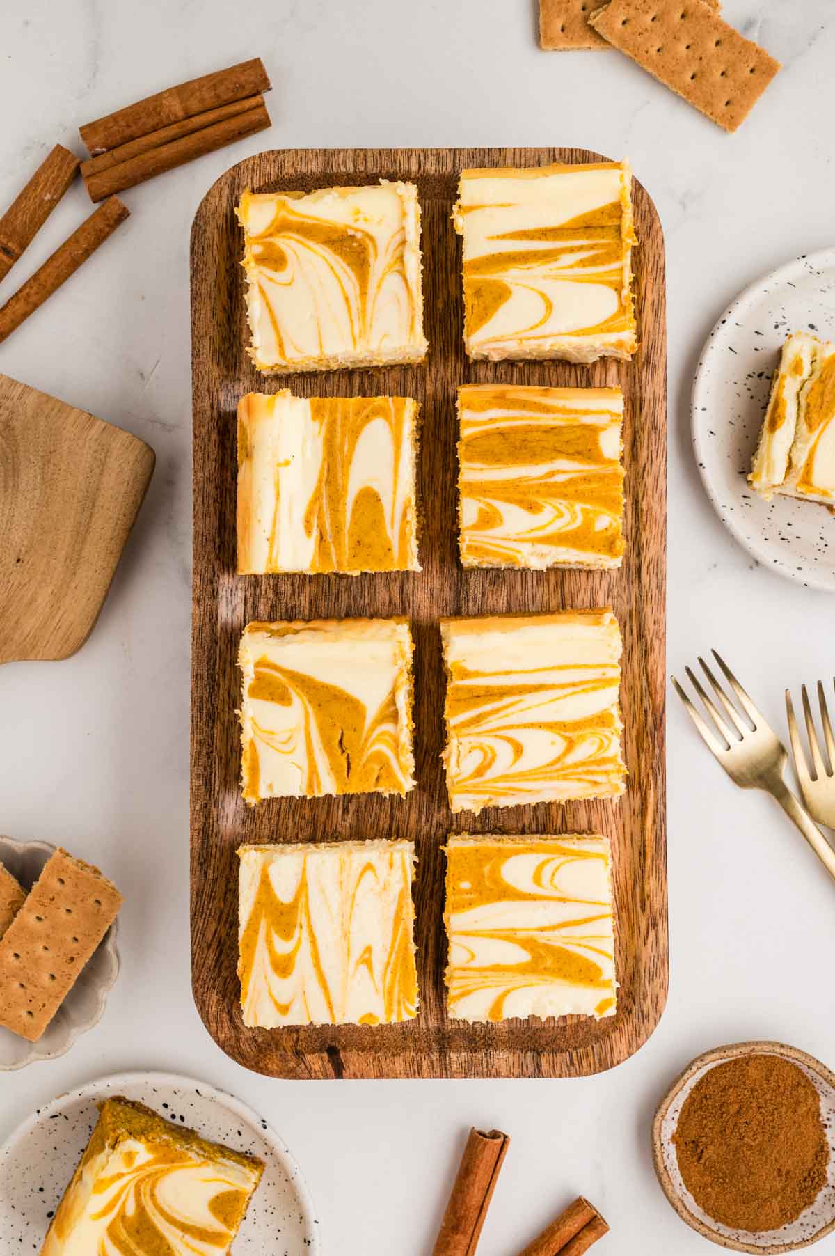 Pumpkin cheesecake bars on a wooden board wit two bars on plates next to it.