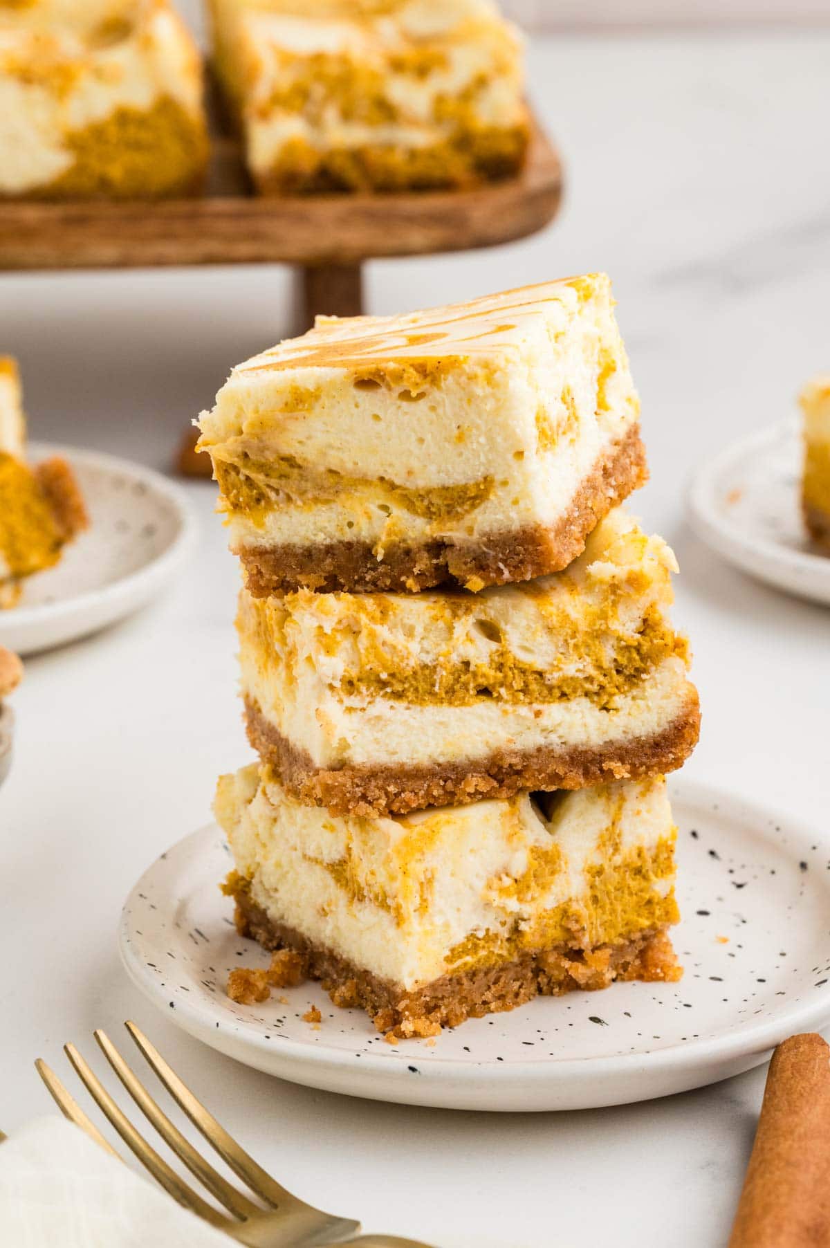 Three pumpkin cheesecake bars stacked on top of each other on a plate.