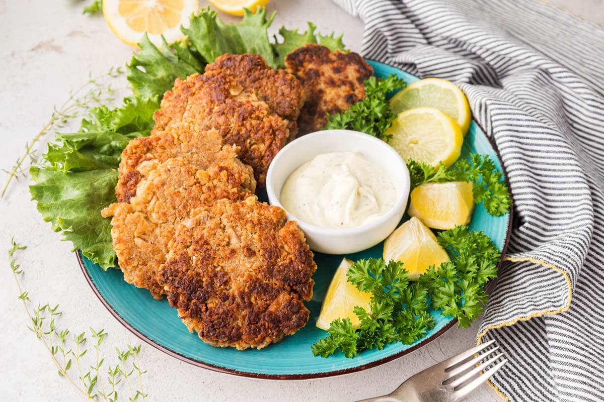 Salmon patties on a blue plate with tarter sauce and lemon wedges.