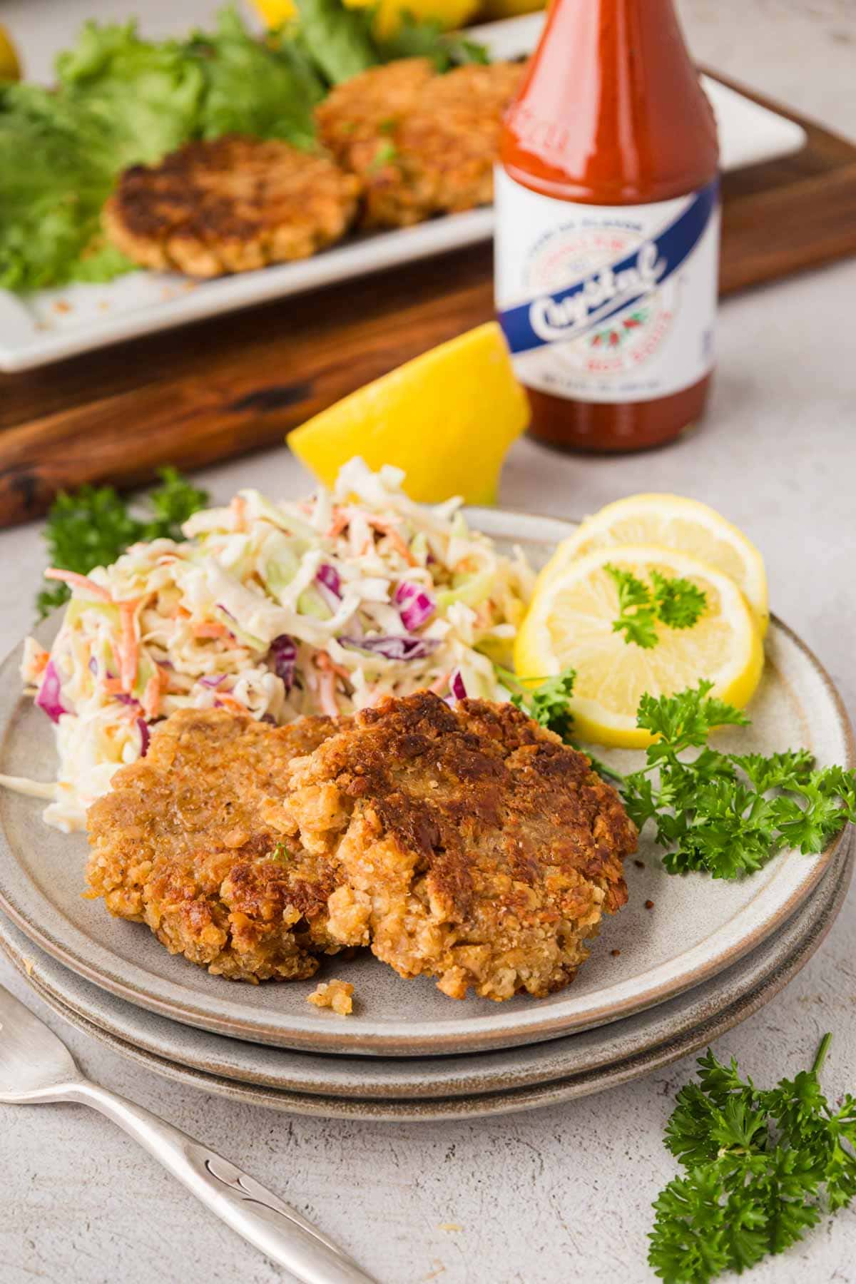 Salmon patties on a plate with coleslaw and lemon slices.