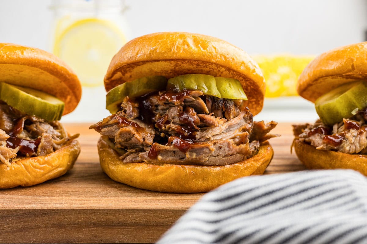 A wooden board with three pulled pork barbecue sandwiches.
