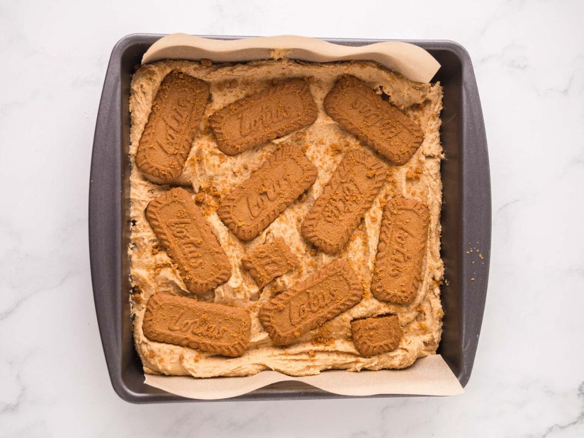 Cookie dough layered in a baking sheet with biscoff cookies layered on top.
