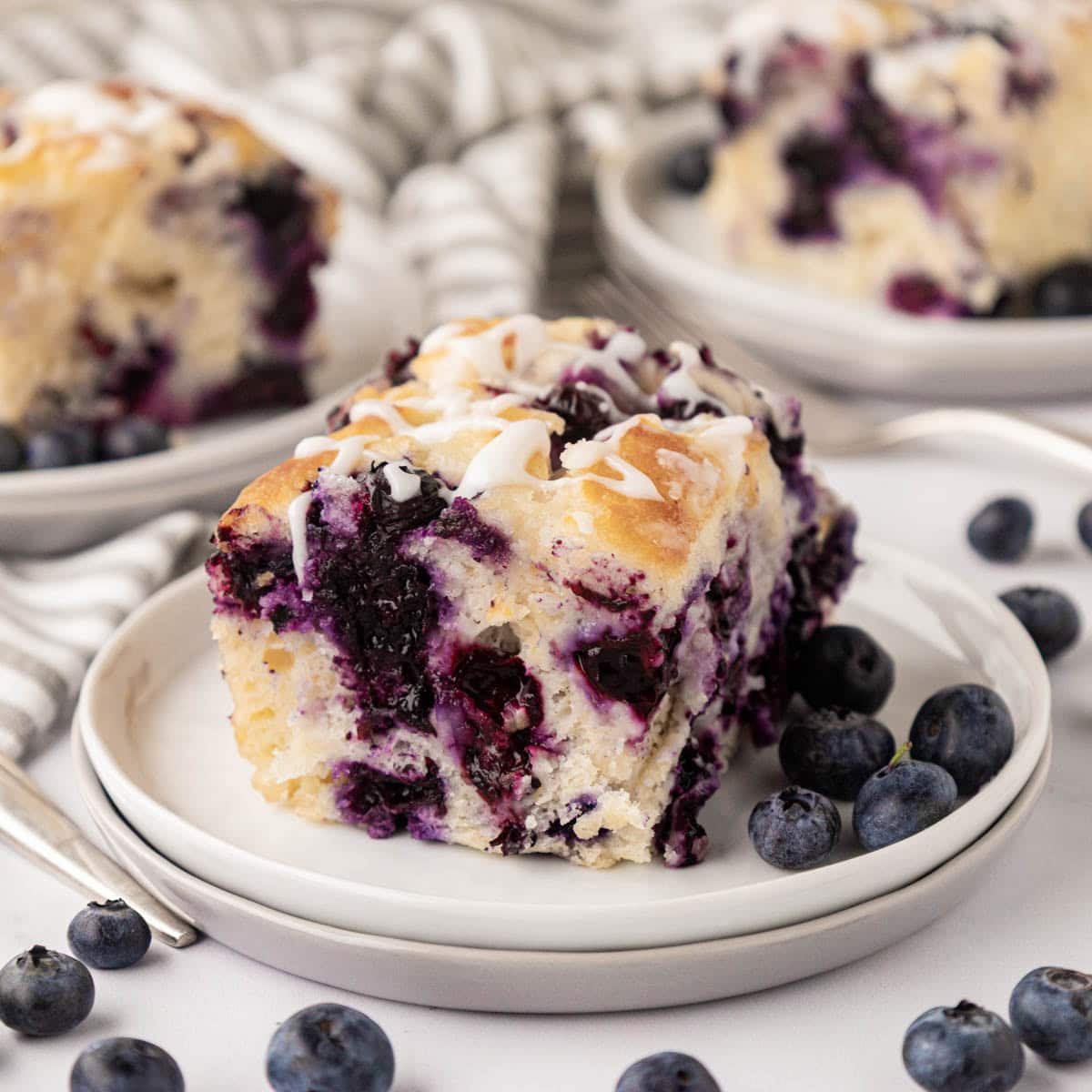 A blueberry butter swim biscuit on a white plate with blueberries.
